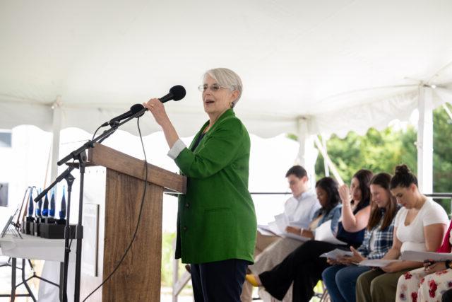 一个灰色头发，穿着绿色西装的女人站在讲台上